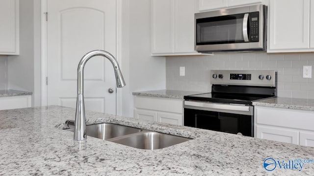 kitchen featuring sink, appliances with stainless steel finishes, backsplash, light stone counters, and white cabinets