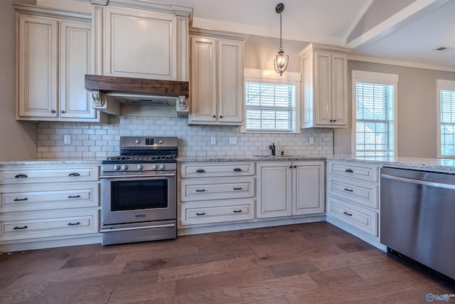 kitchen featuring tasteful backsplash, cream cabinetry, stainless steel appliances, pendant lighting, and dark wood-type flooring