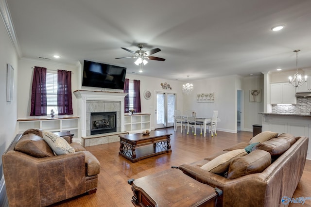 living room with crown molding, ceiling fan with notable chandelier, a tile fireplace, and light wood-type flooring