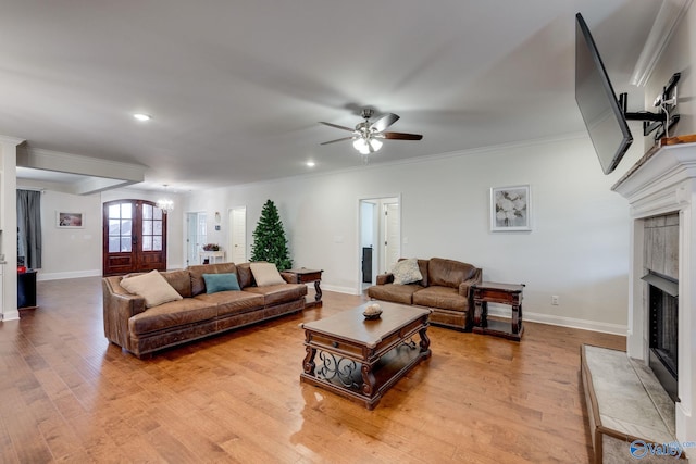 living room featuring a tiled fireplace, ornamental molding, light wood-type flooring, and french doors