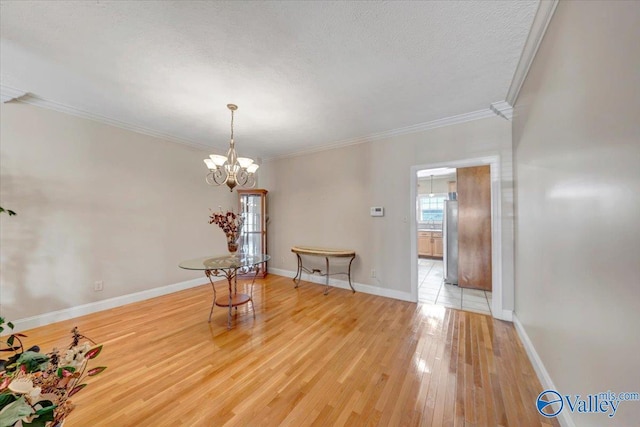 unfurnished dining area with ornamental molding, baseboards, light wood-type flooring, a notable chandelier, and a textured ceiling