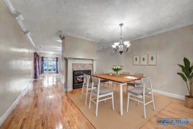 dining space featuring a tile fireplace, an inviting chandelier, light wood-style floors, ornamental molding, and baseboards