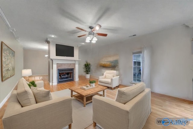 living room featuring a tile fireplace, light wood-style floors, a ceiling fan, and visible vents