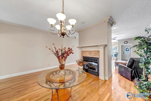 living area featuring a tile fireplace, ornamental molding, light wood finished floors, a notable chandelier, and a textured ceiling