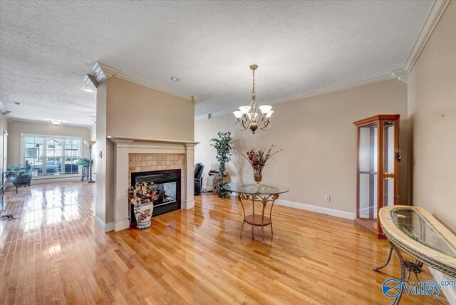 living room featuring a tile fireplace, light wood-style floors, a textured ceiling, and crown molding