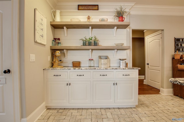 bar with white cabinetry, ornamental molding, and light stone countertops