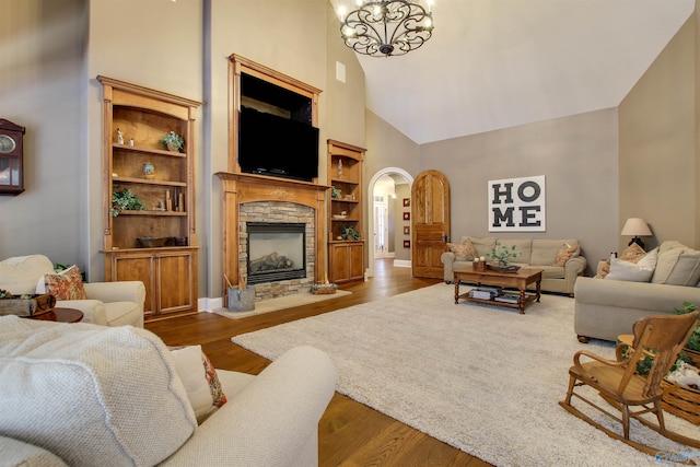 living room featuring a towering ceiling, hardwood / wood-style floors, a stone fireplace, and an inviting chandelier