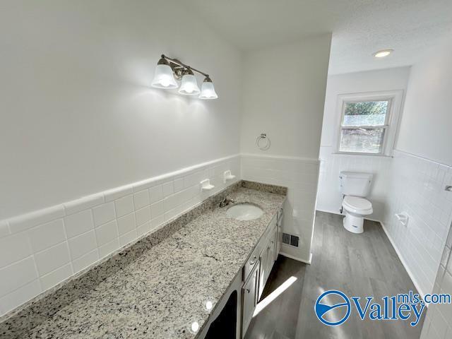 bathroom with toilet, vanity, tile walls, and hardwood / wood-style flooring