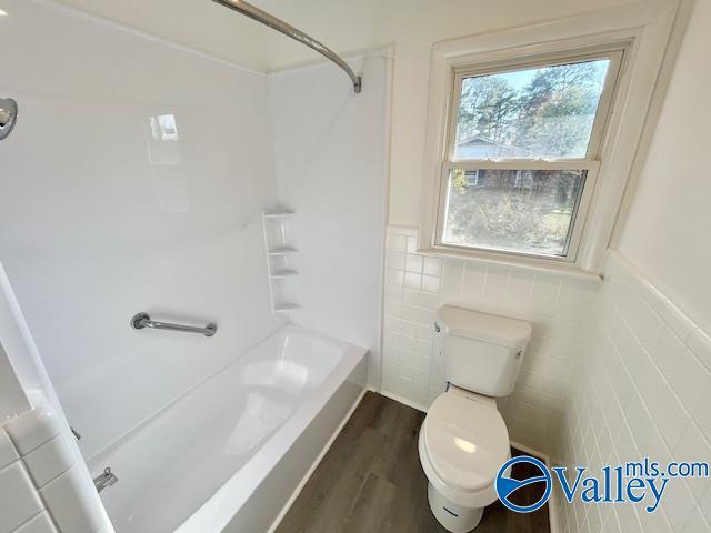 bathroom with hardwood / wood-style floors, toilet, tile walls, and shower / tub combination