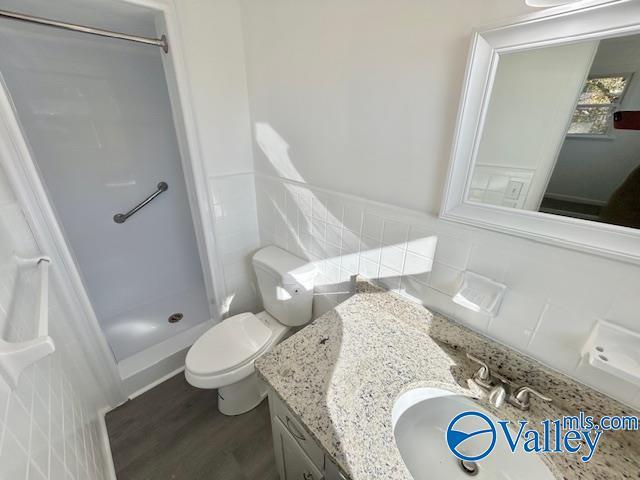 bathroom featuring vanity, a shower, tile walls, hardwood / wood-style floors, and toilet