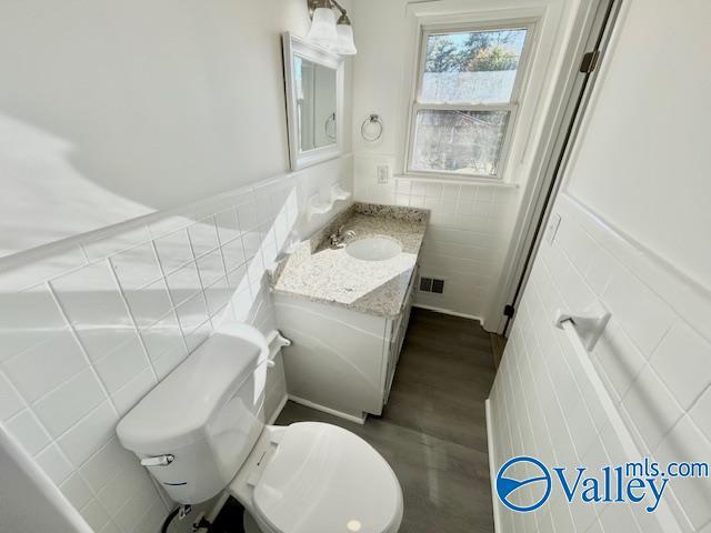 bathroom featuring vanity, hardwood / wood-style flooring, toilet, and tile walls