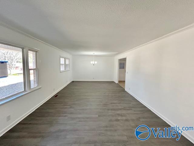 unfurnished room featuring a textured ceiling, a notable chandelier, crown molding, and dark wood-type flooring