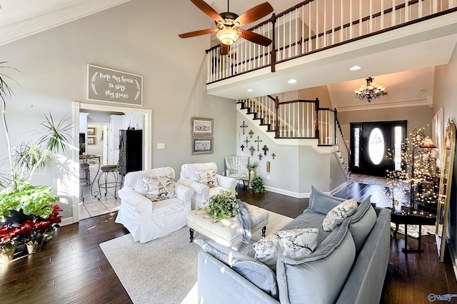 living room featuring dark hardwood / wood-style flooring, ceiling fan with notable chandelier, ornamental molding, and a high ceiling