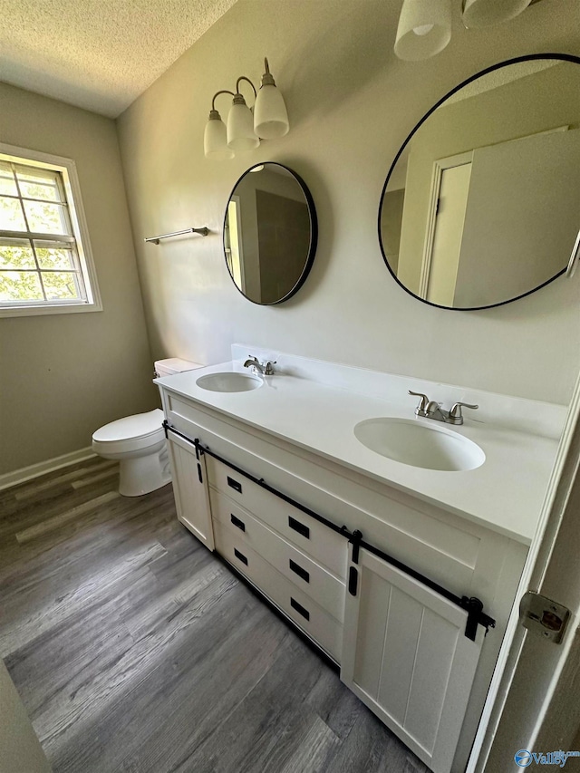 bathroom with a textured ceiling, dual vanity, toilet, and hardwood / wood-style flooring