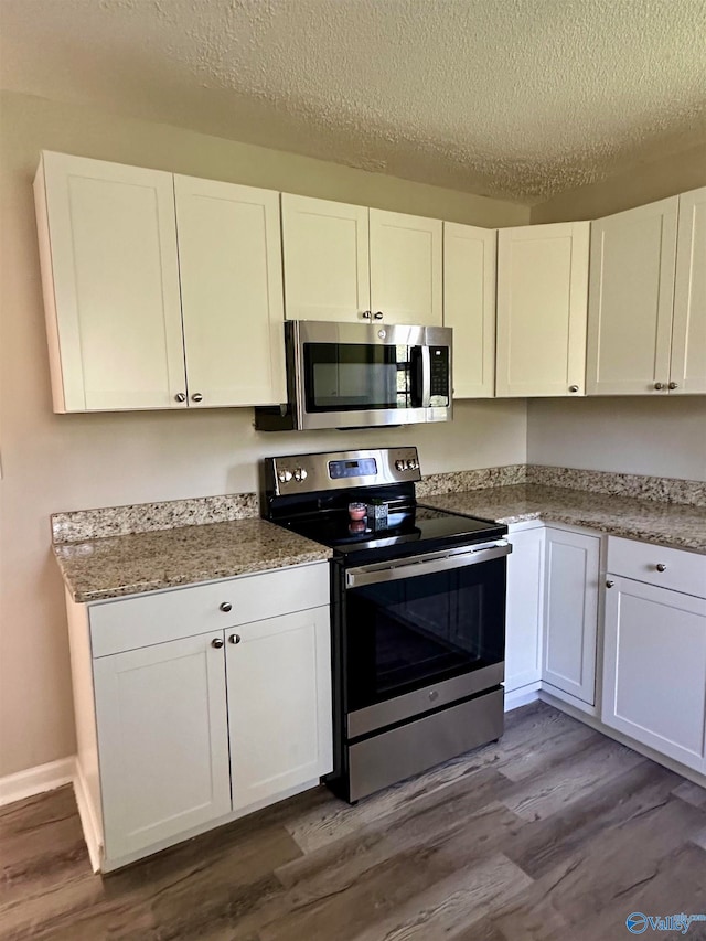 kitchen with appliances with stainless steel finishes, wood-type flooring, a textured ceiling, and white cabinets