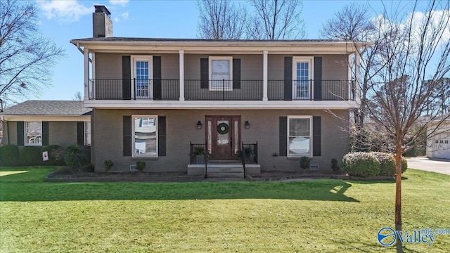 view of property with a front yard, brick siding, a chimney, and a balcony