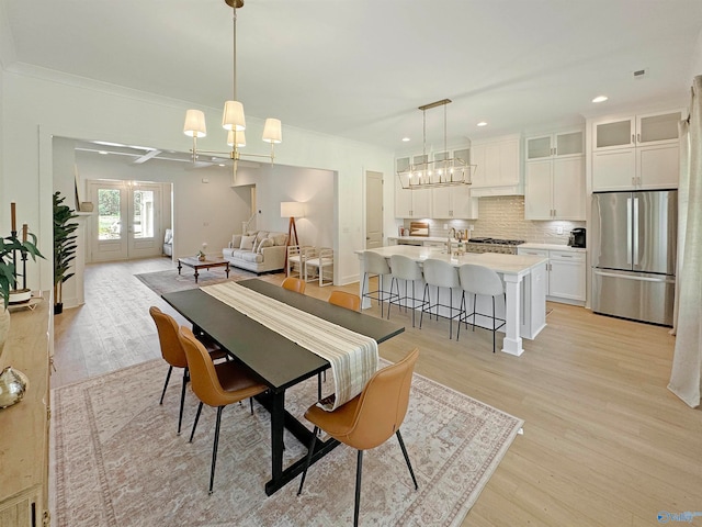 dining area featuring sink, light hardwood / wood-style flooring, an inviting chandelier, ornamental molding, and french doors