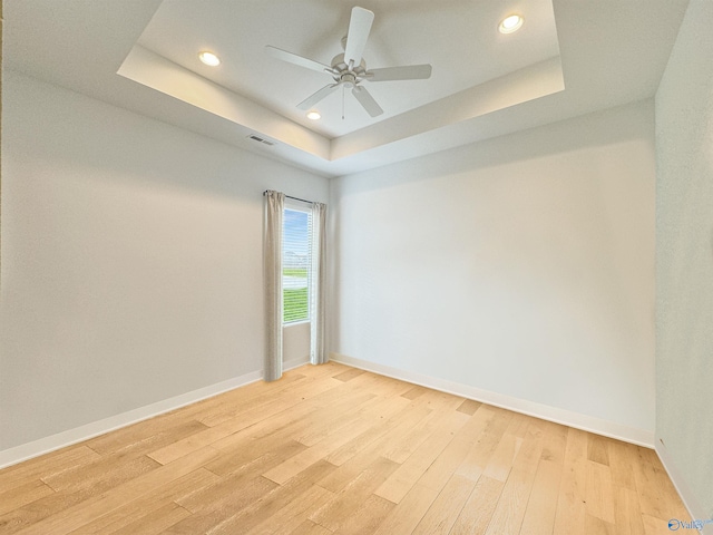 spare room with a tray ceiling, ceiling fan, and light hardwood / wood-style flooring