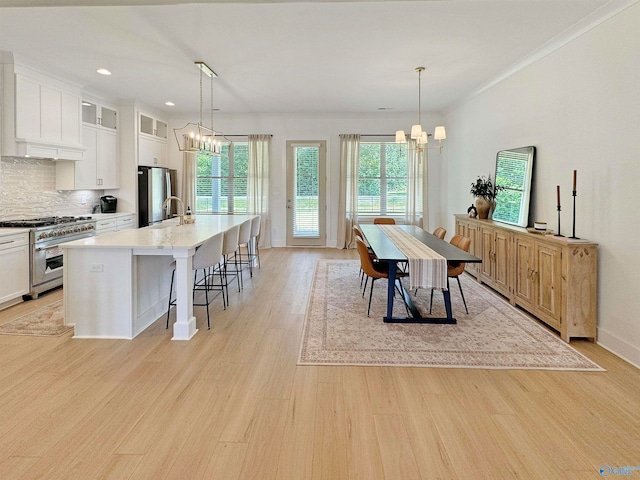 kitchen with a kitchen island with sink, white cabinets, light hardwood / wood-style flooring, stainless steel appliances, and decorative light fixtures