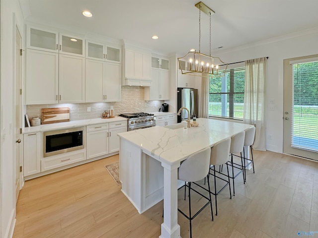 kitchen featuring a chandelier, a kitchen island with sink, white cabinetry, stainless steel appliances, and light stone countertops