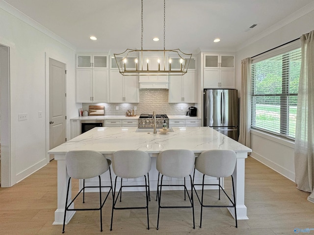 kitchen featuring ornamental molding, white cabinetry, a kitchen island with sink, and stainless steel fridge