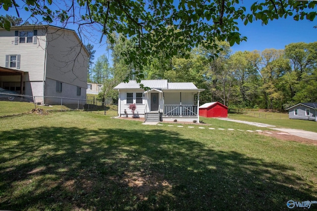 view of front facade featuring fence, covered porch, an outbuilding, and a front yard