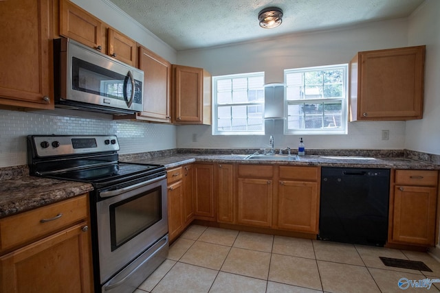 kitchen featuring a textured ceiling, brown cabinets, a sink, backsplash, and stainless steel appliances