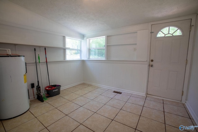 foyer featuring visible vents, a textured ceiling, light tile patterned floors, vaulted ceiling, and electric water heater