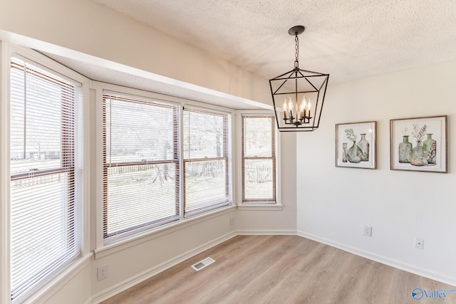 spare room featuring a wealth of natural light, light hardwood / wood-style flooring, a textured ceiling, and a chandelier