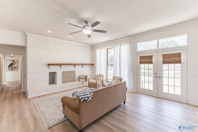 living room featuring a fireplace, a textured ceiling, brick wall, light wood-type flooring, and french doors