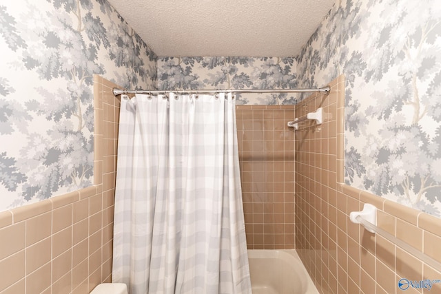 bathroom featuring shower / bath combo with shower curtain, a textured ceiling, and tile walls