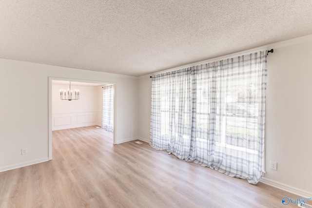 spare room featuring light hardwood / wood-style floors, a textured ceiling, a notable chandelier, and ornamental molding