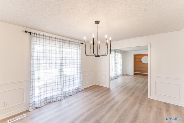 unfurnished dining area featuring a textured ceiling, light hardwood / wood-style flooring, ornamental molding, and a notable chandelier