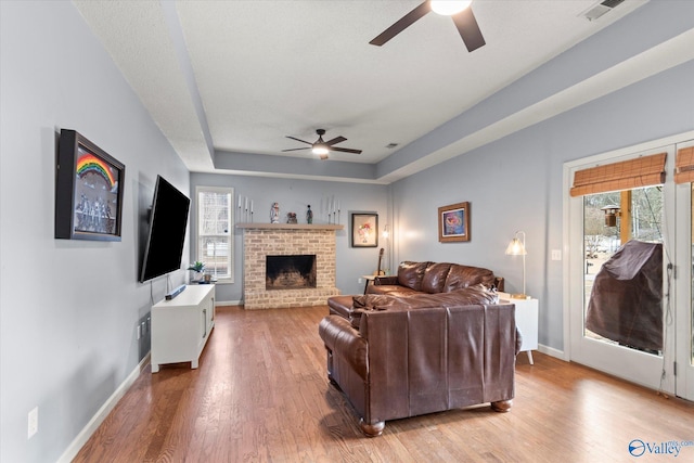 living room featuring light hardwood / wood-style flooring, ceiling fan, a tray ceiling, a fireplace, and a textured ceiling