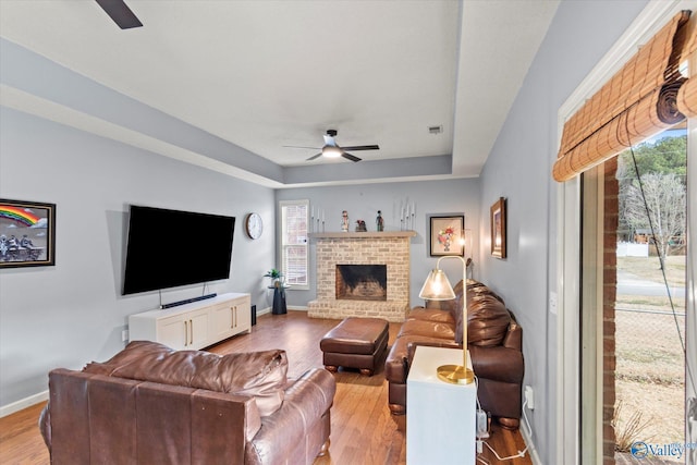 living room featuring ceiling fan, a fireplace, light wood-type flooring, and a tray ceiling