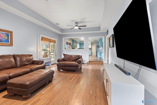 living room featuring ceiling fan, a raised ceiling, and light wood-type flooring