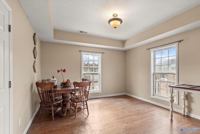 dining room with wood-type flooring, a tray ceiling, and a textured ceiling