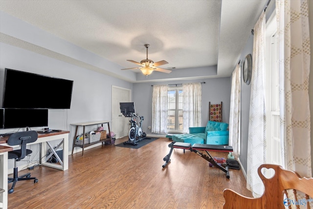 workout room with ceiling fan, wood-type flooring, a raised ceiling, and a textured ceiling