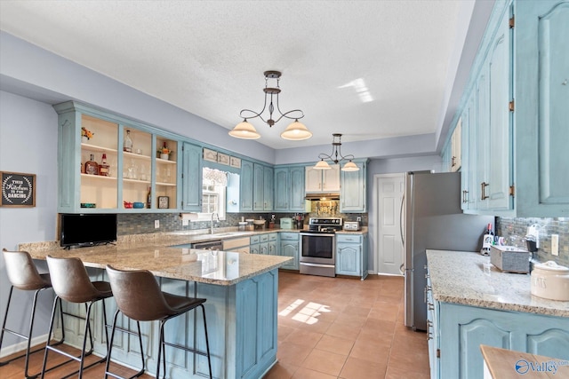 kitchen featuring appliances with stainless steel finishes, decorative light fixtures, sink, kitchen peninsula, and light stone countertops