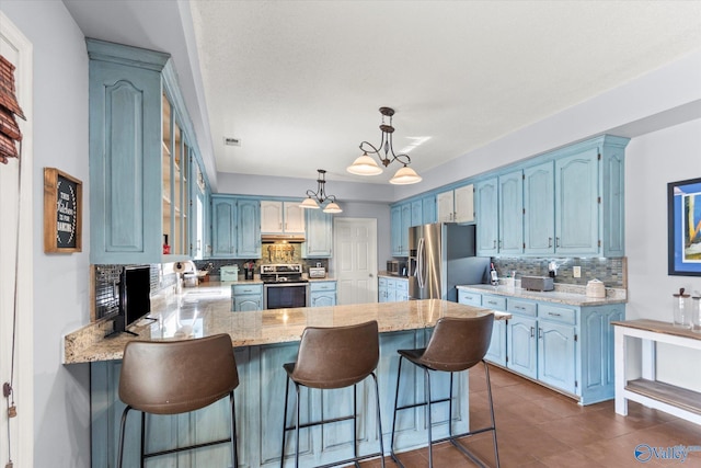 kitchen with decorative backsplash, appliances with stainless steel finishes, a notable chandelier, and kitchen peninsula