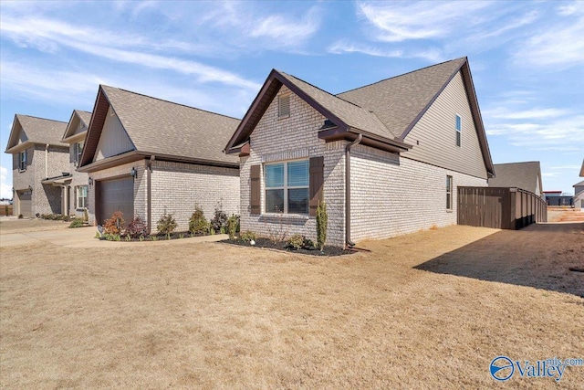 view of side of home with concrete driveway, brick siding, an attached garage, and a shingled roof