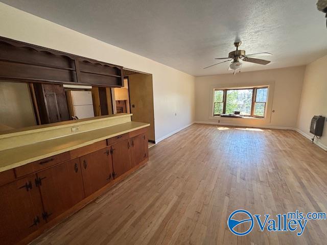 unfurnished living room with light wood-style flooring, heating unit, baseboards, and ceiling fan
