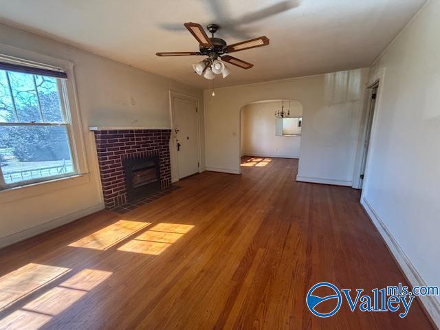 unfurnished living room featuring baseboards, ceiling fan, a tile fireplace, wood finished floors, and arched walkways