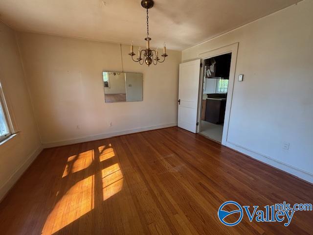 unfurnished room with baseboards, an inviting chandelier, and wood finished floors