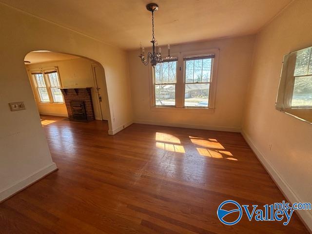 unfurnished dining area with wood finished floors, baseboards, an inviting chandelier, arched walkways, and a brick fireplace
