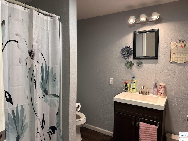 bathroom featuring baseboards, toilet, a textured wall, wood finished floors, and vanity