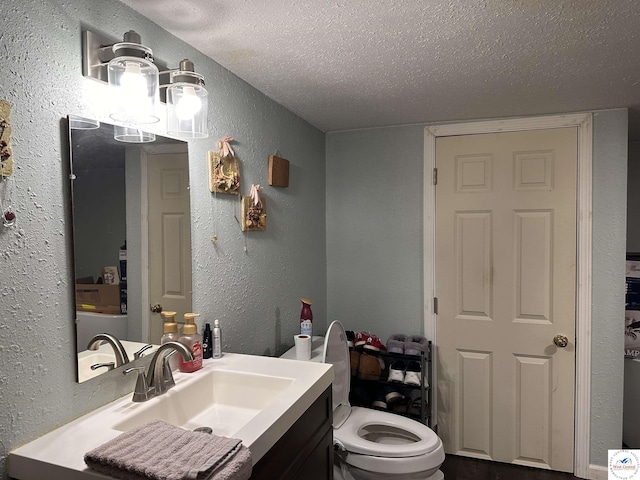 bathroom with vanity, toilet, a textured wall, and a textured ceiling