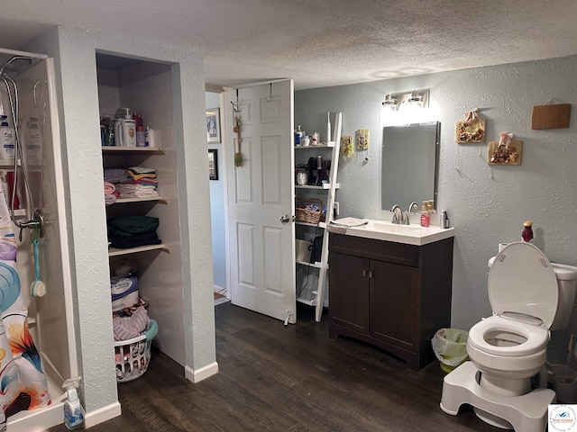 full bathroom featuring vanity, wood finished floors, a shower stall, a textured ceiling, and a textured wall