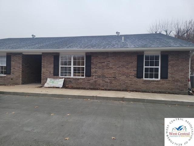 view of front of property with brick siding, roof with shingles, and a patio area