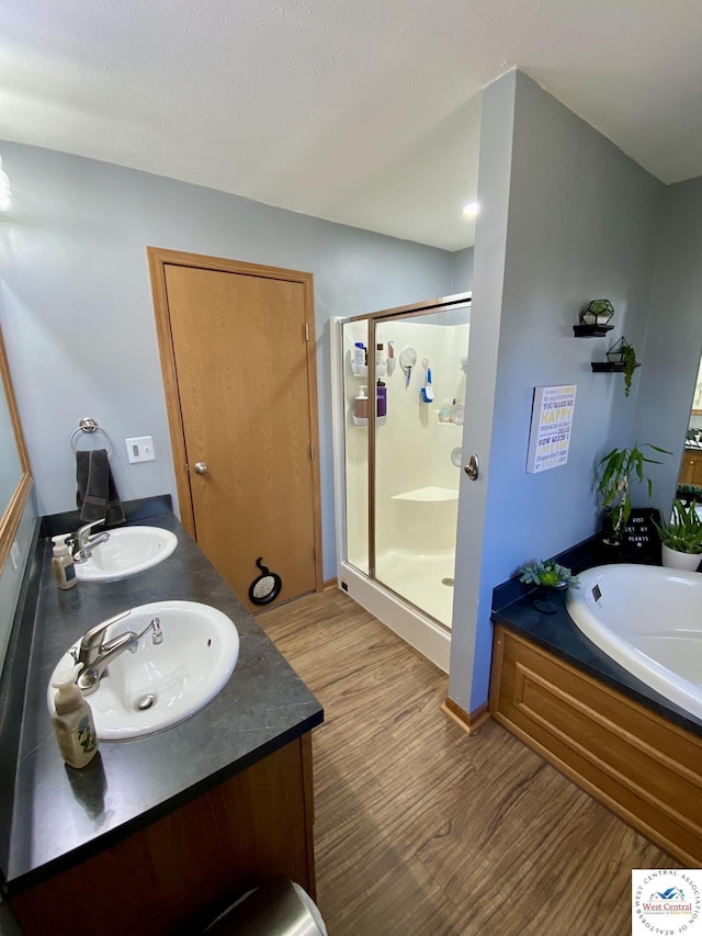 bathroom featuring a stall shower, a garden tub, a sink, and wood finished floors